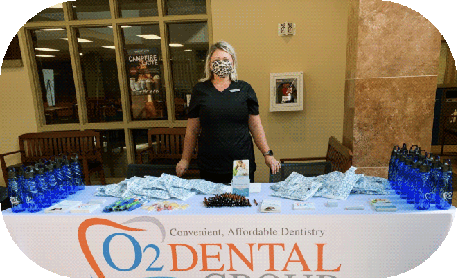 O2 Dental Group staff member at a community booth featuring promotional giveaways and "Affordable Dentistry" signage.
