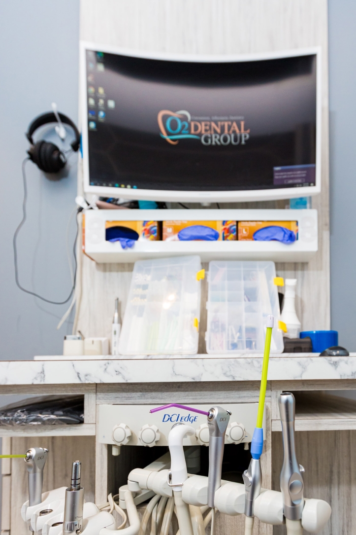 Modern dental treatment room equipped with clinical instruments, featuring the O2 Dental Group logo on the monitor.